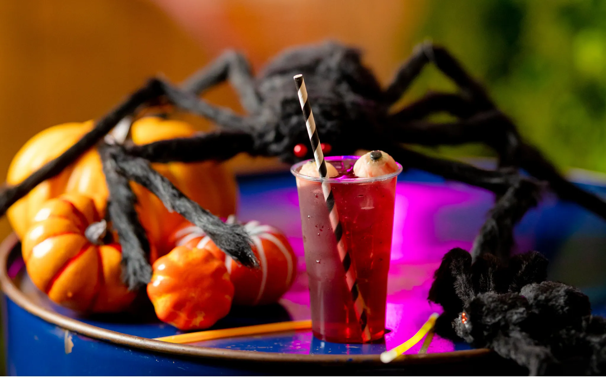 Cocktail sitting on a barrel with large spiders and pumpkins in the background