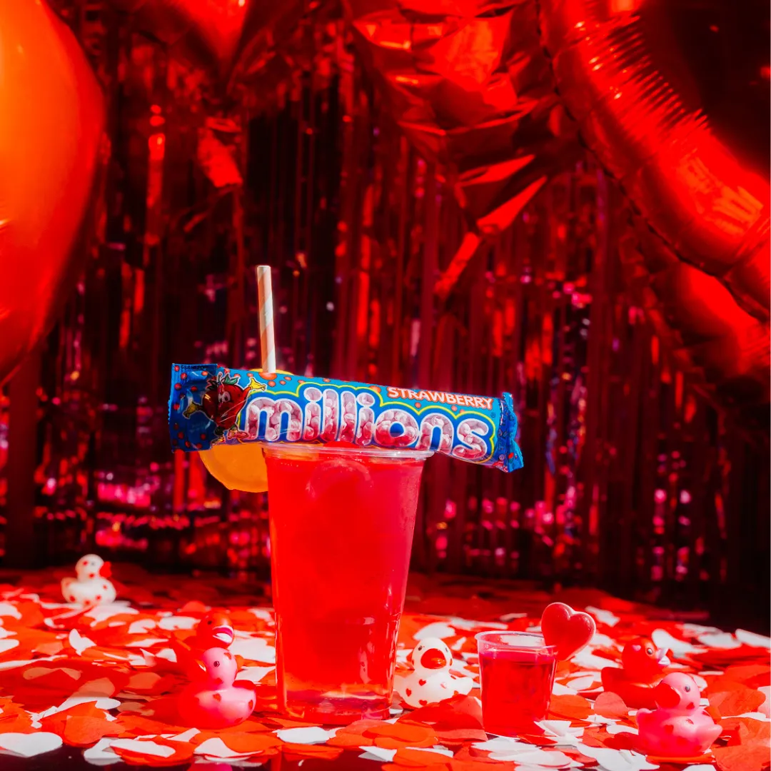 Pink cocktail and shot sitting on confetti covered table in front of heart balloons